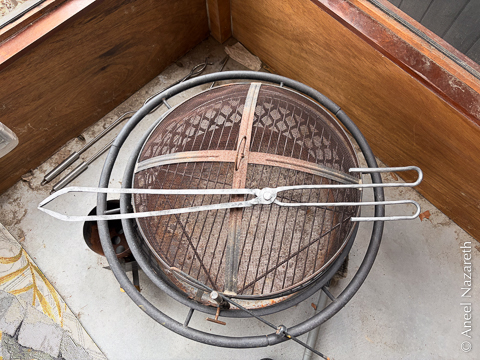 A pair of long tongs with the pivot in the middle, laid across a fire pit